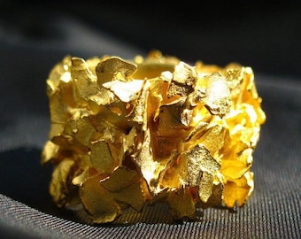May include: A chunky gold ring with a textured, organic design. The ring is made of many small, irregular pieces of gold that are joined together to create a unique and eye-catching look.