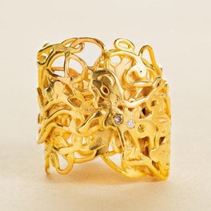 May include: A gold ring with a delicate, intricate design featuring a swirling, organic pattern. The ring is set with three small diamonds.