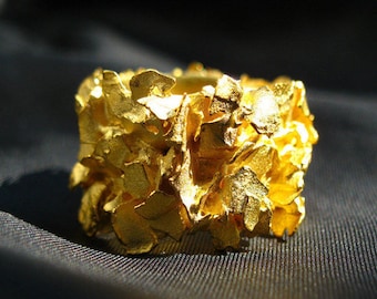 May include: A gold ring with a textured, organic design. The ring is made of many small, irregular pieces of gold that are joined together to create a unique and eye-catching look.