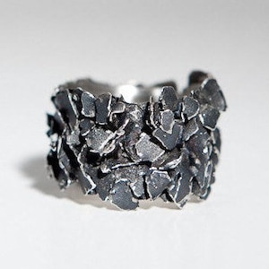 May include: A silver ring with a textured, rough surface, resembling a cluster of small, irregular shapes.