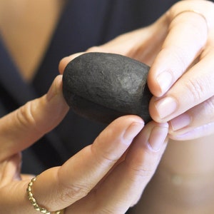 May include: A person is holding a smooth, black, oval-shaped stone in their hands.