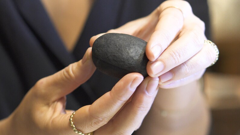 May include: A person is holding a smooth, black, oval-shaped stone in their hands.