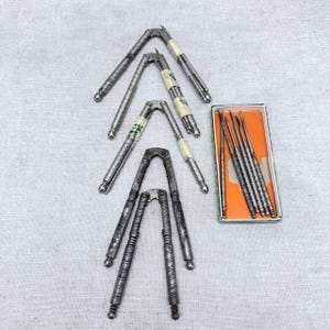 May include: A collection of three metal nutcrackers with textured handles and a rectangular box containing six thin metal picks. The nutcrackers are arranged in a vertical row, each featuring a hinged design, while the picks are stored inside.