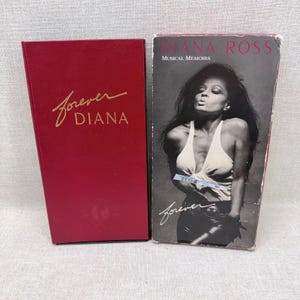 Könnte beinhalten: Eine rote Box mit goldfarbenem Schriftzug "Forever DIANA" neben einem Buch mit einem Schwarz-Weiß-Foto von Diana Ross. Das Buch trägt den Titel "DIANA ROSS Musical Memoirs" mit dem Wort "Forever" in Schreibschrift.
