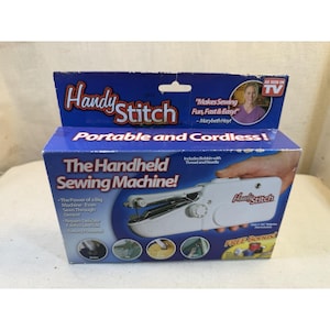 May include: A white handheld sewing machine in a blue cardboard box labelled Handy Stitch. The packaging features the text Portable and Cordless, The Handheld Sewing Machine, and As Seen On TV, along with images of the device sewing various fabrics.