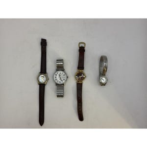May include: Four wristwatches arranged in a row. The first has a dark brown strap and silver case. The second features a silver-tone metal expansion band and white dial. The third has a dark brown strap and gold-tone case. The fourth has a silver-tone expansion band.