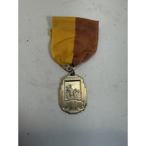 May include: A silver-toned rectangular medal featuring a relief of a swimmer in water, suspended from a vertically split yellow and brown grosgrain ribbon. The medal has a stepped, geometric border design and a blank rectangular space at the bottom.
