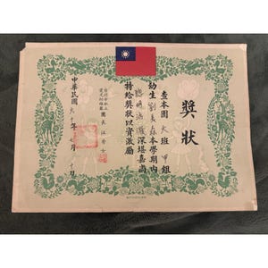 May include: A vintage certificate with Chinese characters and a small flag. The certificate has a green border with floral and animal designs. The text is in black and red, with a stamp and the date.