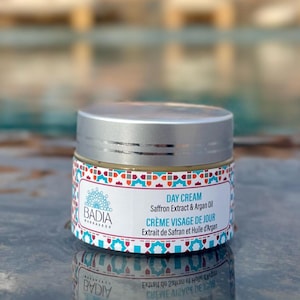 May include: A round jar of Badia Marrakech day cream with a silver lid. The label features a colorful geometric pattern in red, blue, and white, with text reading Day Cream, Saffron Extract & Argan Oil, and Crème Visage de Jour.