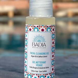May include: A clear plastic pump bottle of Badia Marrakesh facial cleansing gel with a white label featuring a geometric border in red, blue, and teal. The text reads Badia Marrakesh, Facial Cleansing Gel, Argan Oil & Saffron Extract, Gel Nettoyant Visage, Huile d'Argan et Extrait de Safran, and Sulfate Free - Sans Sulfate.