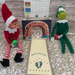 May include: A Christmas-themed display featuring two elf dolls, a miniature bowling alley with the text "North Pole Lanes", and a bowling score sheet. The elf on the left is red and white, holding a green ball. The other elf is green and holding a red ball.