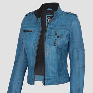 May include: A teal blue leather jacket with a stand-up collar and multiple zippered pockets. The jacket features a front zipper closure, shoulder epaulets, and a black interior lining. The leather has a distressed appearance.