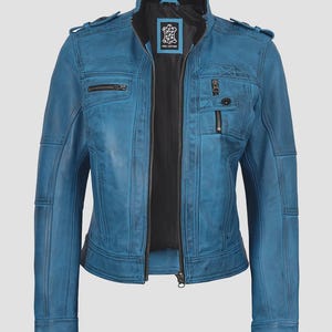 May include: A teal blue leather jacket with a black interior lining. The jacket features a zip-up front, multiple pockets with zippers, and a stand-up collar. The shoulders have decorative stitching and small flaps. The jacket is a classic style.