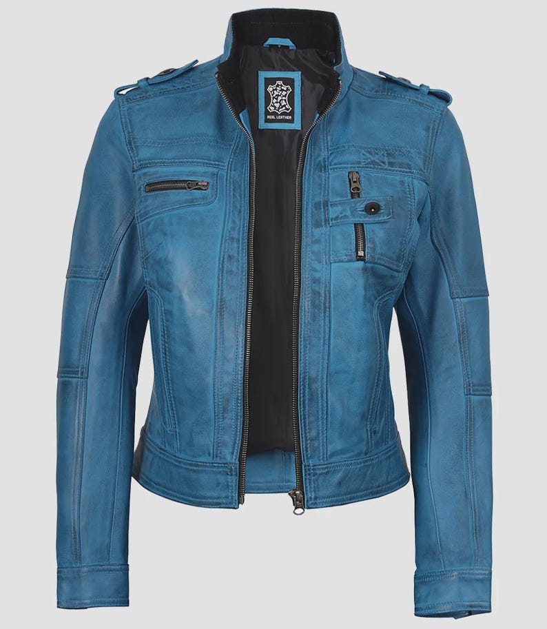 May include: A teal blue leather jacket with a black interior lining. The jacket features a zip-up front, multiple pockets with zippers, and a stand-up collar. The shoulders have decorative stitching and small flaps. The jacket is a classic style.
