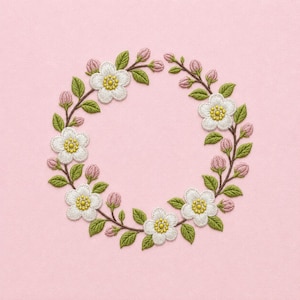 May include: An embroidered circular wreath featuring white five-petaled flowers with yellow centers, interspersed with small pink flower buds and green leaves on thin brown stems, arranged in a continuous ring pattern on a solid light pink background.