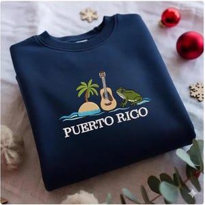 May include: Navy blue sweatshirt with embroidered design featuring a tropical island with a palm tree, a guitar, and a green frog. The text "PUERTO RICO" is embroidered below the design.