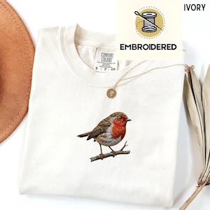 Embroidered robin bird shirt featuring a small red-breasted bird perched on a branch in a minimal nature-inspired design.