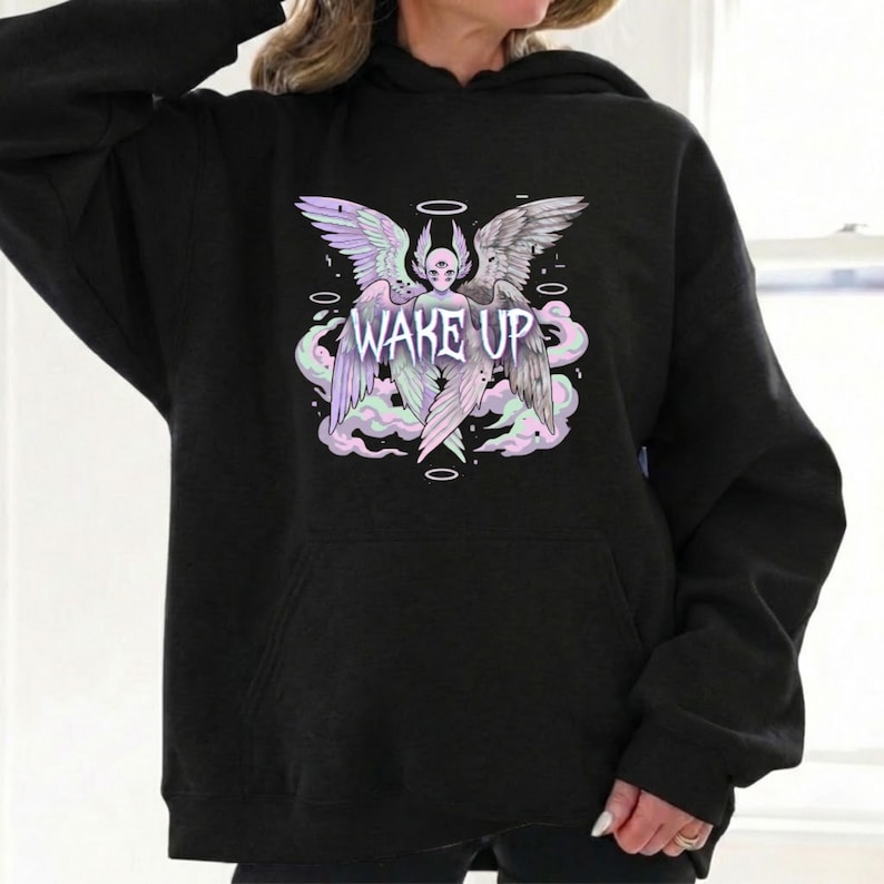 May include: Black hoodie with a graphic design. The design features a winged figure with a halo, clouds, and the text "WAKE UP". The graphic uses pastel colours including purple, pink, and green.
