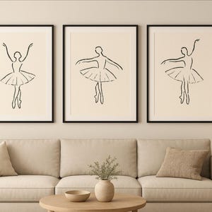May include: Three framed art prints featuring minimalist line drawings of ballerinas in various poses. Each ballerina is depicted in black ink on a cream-colored background, with a black frame. The artwork is displayed above a beige sofa.