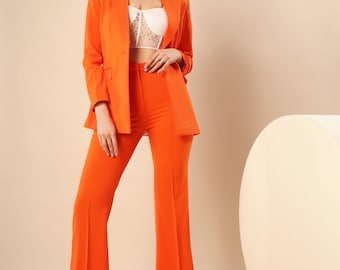 May include: A vibrant orange blazer and matching flared pants. The blazer has a classic lapel and a single-button closure. The pants have a high waist and a wide leg. The outfit is paired with a white lace top and cream-colored shoes. The ensemble is a bold fashion statement.