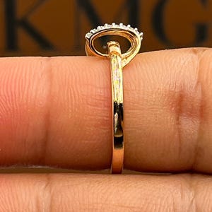 May include: A gold ring with a black oval stone and a halo of small white stones. The ring is held between fingers, showcasing the polished gold band and the intricate setting of the gemstones.