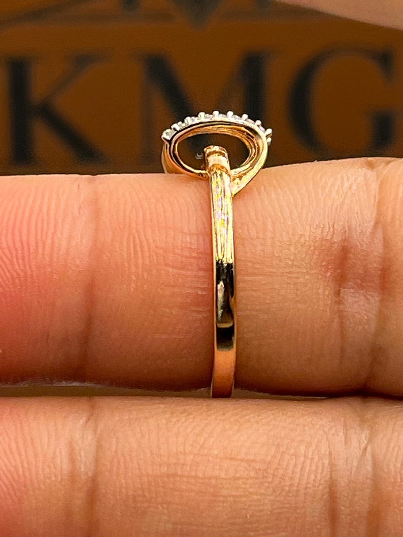 May include: A gold ring with a black oval stone and a halo of small white stones. The ring is held between fingers, showcasing the polished gold band and the intricate setting of the gemstones.
