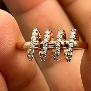 May include: A gold-toned ring featuring three vertical, curved bands encrusted with small, sparkling white stones. The ring's design is modern and eye-catching, with the bands evenly spaced across the top.