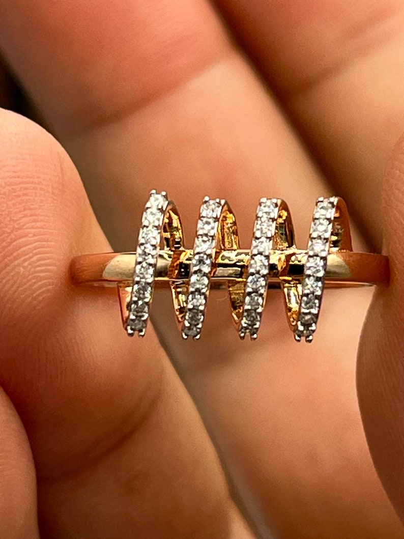 May include: A gold-toned ring featuring three vertical, curved bands encrusted with small, sparkling white stones. The ring's design is modern and eye-catching, with the bands evenly spaced across the top.