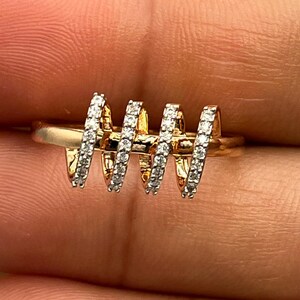 May include: A gold-toned ring with a unique design. The ring features four spiraling sections, each encrusted with small, sparkling stones. The ring is set against a neutral background, highlighting its intricate details and craftsmanship.