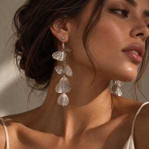 May include: Long drop earrings featuring a series of translucent, petal-shaped elements in a pale silver tone. The earrings are constructed with delicate metal chains connecting each individual leaf-like component, creating a cascading effect that hangs vertically from a small stud post.