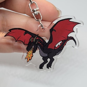 May include: A red and black dragon keychain with a silver chain and clasp. The dragon is breathing fire and has its wings spread out.