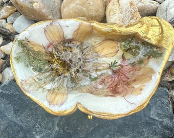 Pequeño plato para joyas con forma de concha de ostra y flores secas.