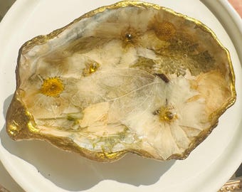 Plato para joyas hecho con conchas de ostras, decorado con flores secas y algunos diamantes de imitación.