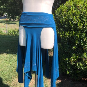 Op de afbeelding: Een tealblauwe rok met een hoge taille en een bloemenpatroon. De rok heeft twee splitten aan de zijkanten en een vloeiende, asymmetrische zoom.