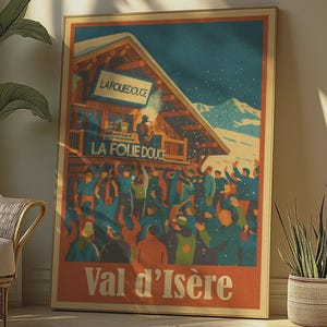 Pode incluir: Um cartaz emoldurado com um tema de viagem vintage. O cartaz apresenta uma multidão de pessoas em frente a um edifício com o texto "LA FOLIE DOUCE" e "Val d'Isère". A paleta de cores inclui tons de azul, laranja e castanho. O cartaz está encostado a uma parede.