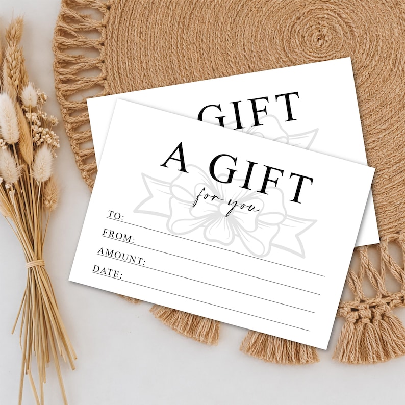 K&ouml;nnte beinhalten: Zwei wei&szlig;e Geschenkkarten mit schwarzem Text, der "A GIFT for you" lautet. Die Karten haben Zeilen f&uuml;r "TO:", "FROM:", "AMOUNT:" und "DATE:". Eine dekorative Schleifengrafik befindet sich in der Mitte. Die Karten liegen auf einem gewebten beigefarbenen Platzset.