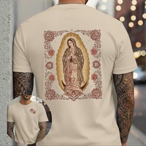 May include: A beige short-sleeve t-shirt featuring a large graphic on the back of the Virgin of Guadalupe surrounded by a floral border. A smaller version of the floral design is printed on the front left chest area of the garment.