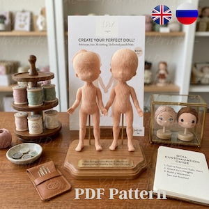 Peut inclure: Deux ébauches de poupées crochetées sur une base en bois, avec une pancarte indiquant "The Amigurumi Blank Collection". Un guide intitulé "Doll Customization Guide" est visible. L'image comprend également des bobines de fil, des boutons et un étui à aiguilles en cuir. Le texte "PDF Pattern" est en bas.