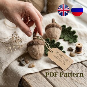 May include: Hand-knitted acorn decor set in beige and brown. The Cozy Grove acorn decor set includes two acorns, a green leaf, and a tag. The tag reads "The Cozy Grove Hand-Knitted Acorn Decor Set". The words "PDF Pattern" are also visible.