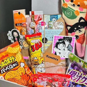 Puede incluir: Una caja blanca llena de snacks y productos de belleza japoneses. Los art&iacute;culos incluyen patatas fritas Calbee, snacks Teriyaki, un tubo de limpiador facial de melocot&oacute;n Naive y calcetines Shiba Inu. La caja tambi&eacute;n contiene pegatinas y otras peque&ntilde;as golosinas.