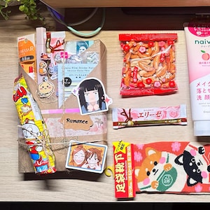Puede incluir: Una colecci&oacute;n de snacks, productos para el cuidado de la piel y art&iacute;culos de papeler&iacute;a japoneses dispuestos sobre una superficie de madera. Incluye bolsas de patatas fritas, un tubo de limpiador facial y un paquete de galletas. Tambi&eacute;n se ven pegatinas decorativas y un par de calcetines Shiba Inu.