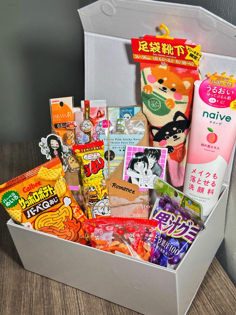 Puede incluir: Una caja blanca llena de snacks y productos de belleza japoneses. Los art&iacute;culos incluyen patatas fritas Calbee, snacks Teriyaki, un tubo de limpiador facial de melocot&oacute;n Naive y calcetines Shiba Inu. La caja tambi&eacute;n contiene pegatinas y otras peque&ntilde;as golosinas.