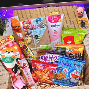 Puede incluir: Una caja de cart&oacute;n llena de aperitivos y productos japoneses. Los art&iacute;culos incluyen un par de calcetines Shiba Inu, un tubo de limpiador facial de extracto de melocot&oacute;n Naive y varios caramelos y galletas envasados. La caja est&aacute; llena de papel de embalaje.