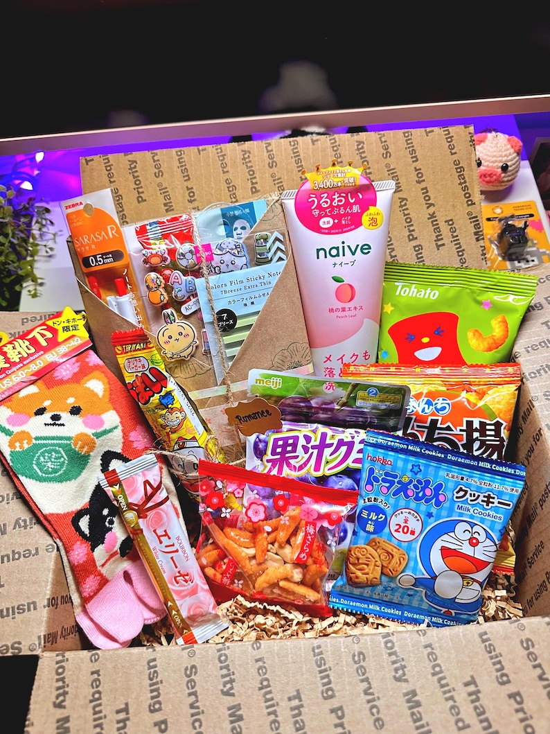 Puede incluir: Una caja de cart&oacute;n llena de aperitivos y productos japoneses. Los art&iacute;culos incluyen un par de calcetines Shiba Inu, un tubo de limpiador facial de extracto de melocot&oacute;n Naive y varios caramelos y galletas envasados. La caja est&aacute; llena de papel de embalaje.