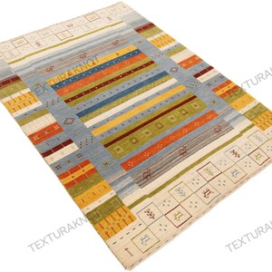 May include: A rectangular area rug with a light blue central field and colorful horizontal stripes in orange, yellow, green, and blue. The rug has a cream-colored border with geometric patterns and is suitable for home decor.