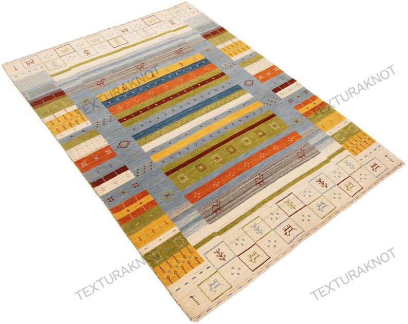 May include: A rectangular area rug with a light blue central field and colorful horizontal stripes in orange, yellow, green, and blue. The rug has a cream-colored border with geometric patterns and is suitable for home decor.