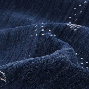 May include: Close-up of a textured, navy blue rug with white dot patterns. The rug's surface has a soft, plush appearance, with visible folds and subtle variations in colour. The design features a repeating pattern of small white dots.