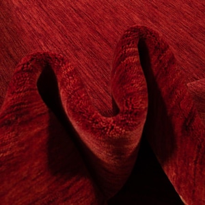 Pu&ograve; includere: Primo piano di un tappeto rosso piegato con una superficie strutturata. Le fibre del tappeto creano un motivo di linee e ombre, con una tonalit&agrave; rosso intenso. Le pieghe aggiungono profondit&agrave; e dimensione al tessuto.