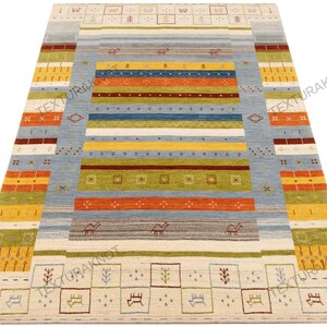 May include: A rectangular area rug with a light blue central field and colorful horizontal stripes in shades of orange, yellow, green, and brown. The rug features geometric patterns and small animal motifs.