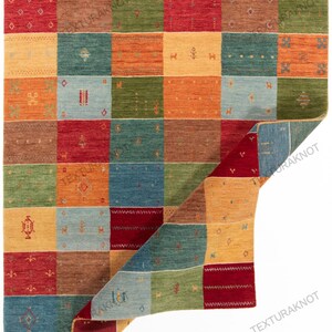 May include: A colorful, rectangular area rug with a patchwork design. The rug features squares in shades of red, orange, yellow, green, and blue. Each square has a unique pattern. The rug is made of a woven material.